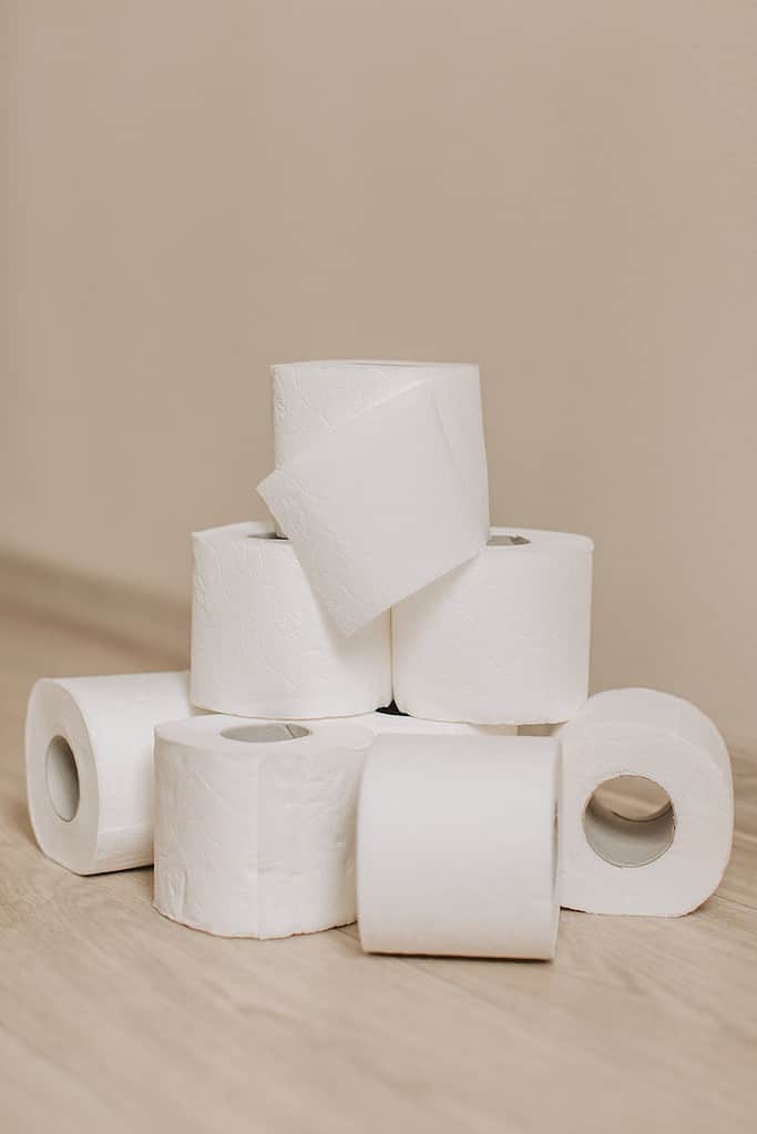 Tower of white toilet paper rolls placed on light wooden floor near wall as everyday need for hygiene and sanitary purposes